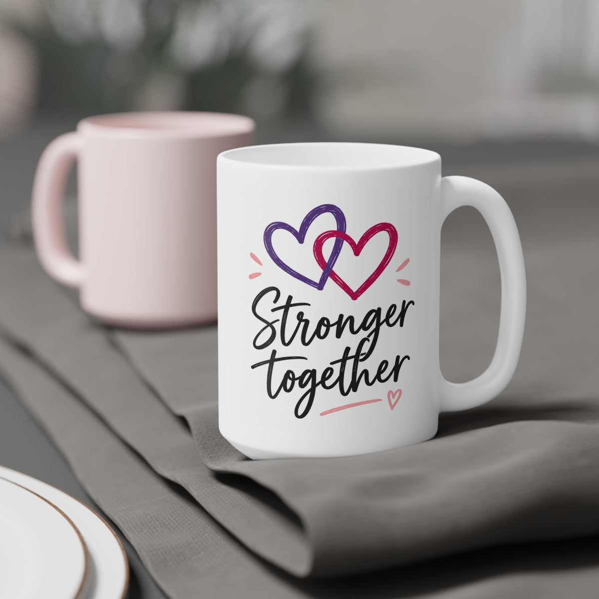White 15oz ceramic mug with Stronger Together lettering and intertwined purple and raspberry hearts, styled product view.