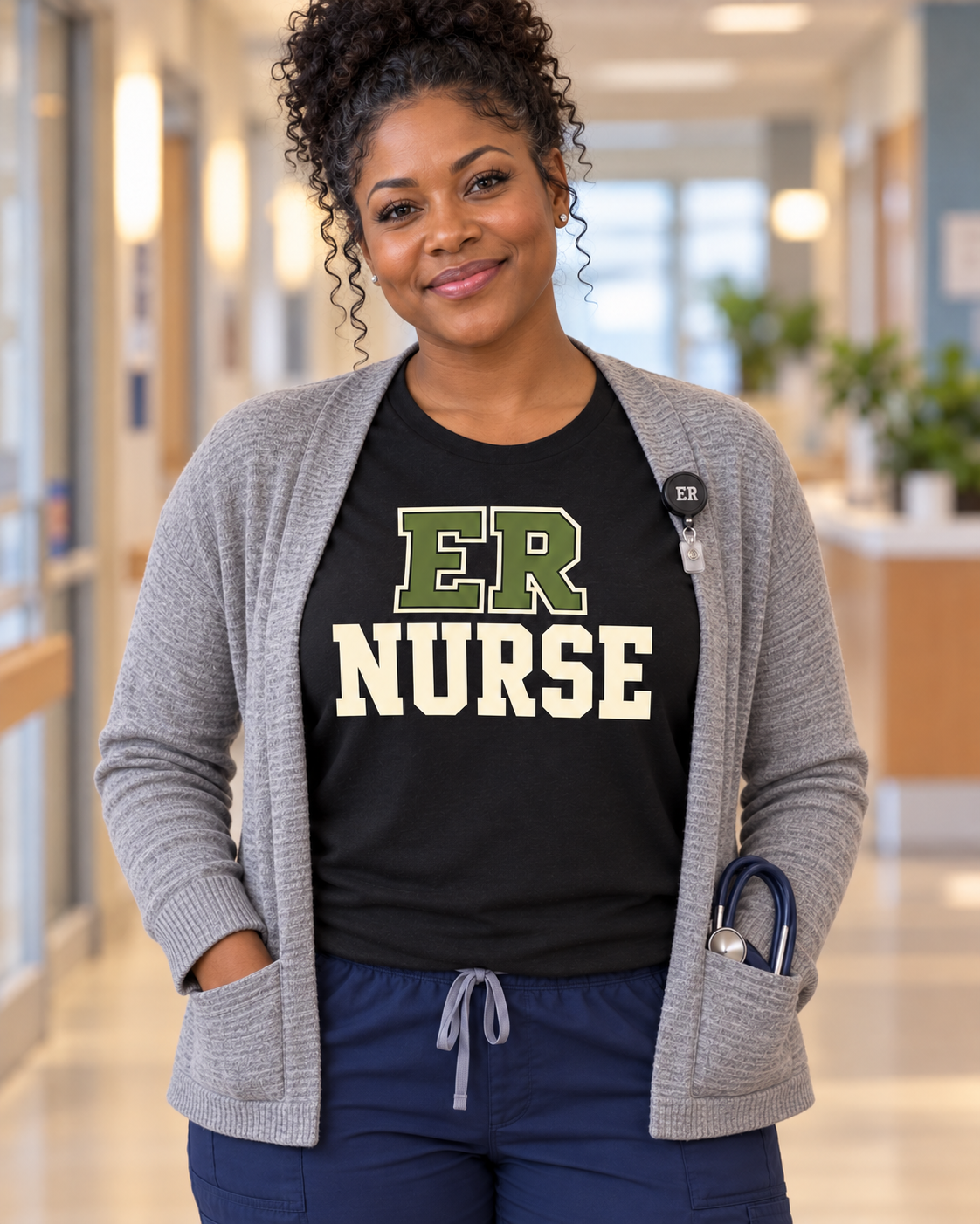 Young nurse wearing a black Nursify ER Nurse shirt under an open grey cardigan, with centred olive and cream collegiate lettering.