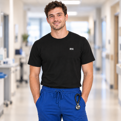 Woman wearing a black RN nurse T-shirt with small white RN lettering high on the left chest, teal joggers and an RN badge reel.