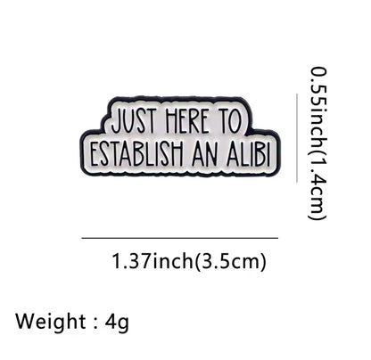 Enamel pin with a white background and bold black lettering reading “Just Here to Establish an Alibi”  approximately 1.37 inches wide and 0.55 Inches long 