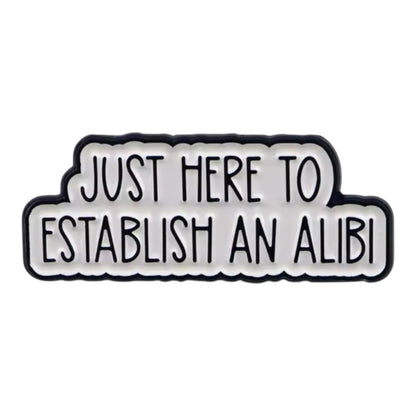 Enamel pin with a white backround and bold black lettering reading “Just Here to Establish an Alibi.”