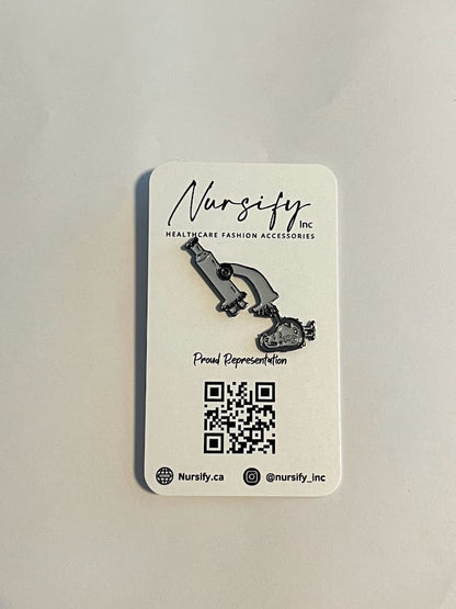 Microscope enamel pin in grey with smiling cell detail | 1.7 cm x 4.2 cm on nursify packaging