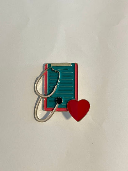 Clipboard stethoscope enamel pin with white and gold stethoscope, pink and teal clipboard, and red heart | 4.8 cm x 5 cm