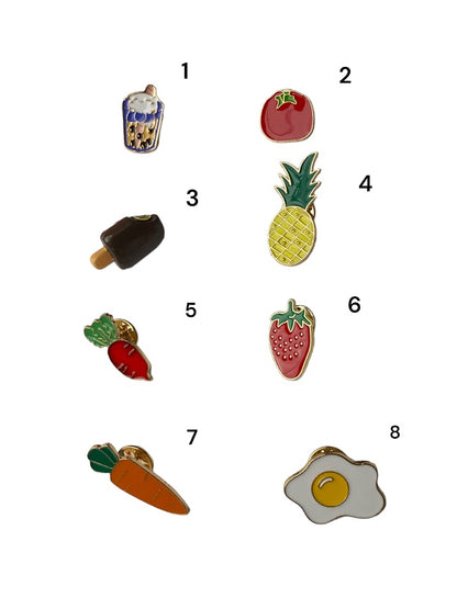 An assortment of food pins all number 1-8 specifically a Tomato pin, Pineapple pin, Strawberry pin, Fried egg, Carrot pin, Beet pin, Boba pin and a Fudgesicle pin. 