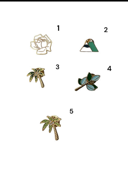a photo of five pins which include a white rose with gold accents a dark green palm tree lighting palm tree mountains and a branch with blue and green leaves number each from 1-5