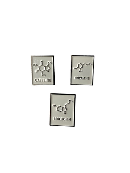 Chemical structure enamel pins for caffeine, dopamine, and serotonin on a white background. 
