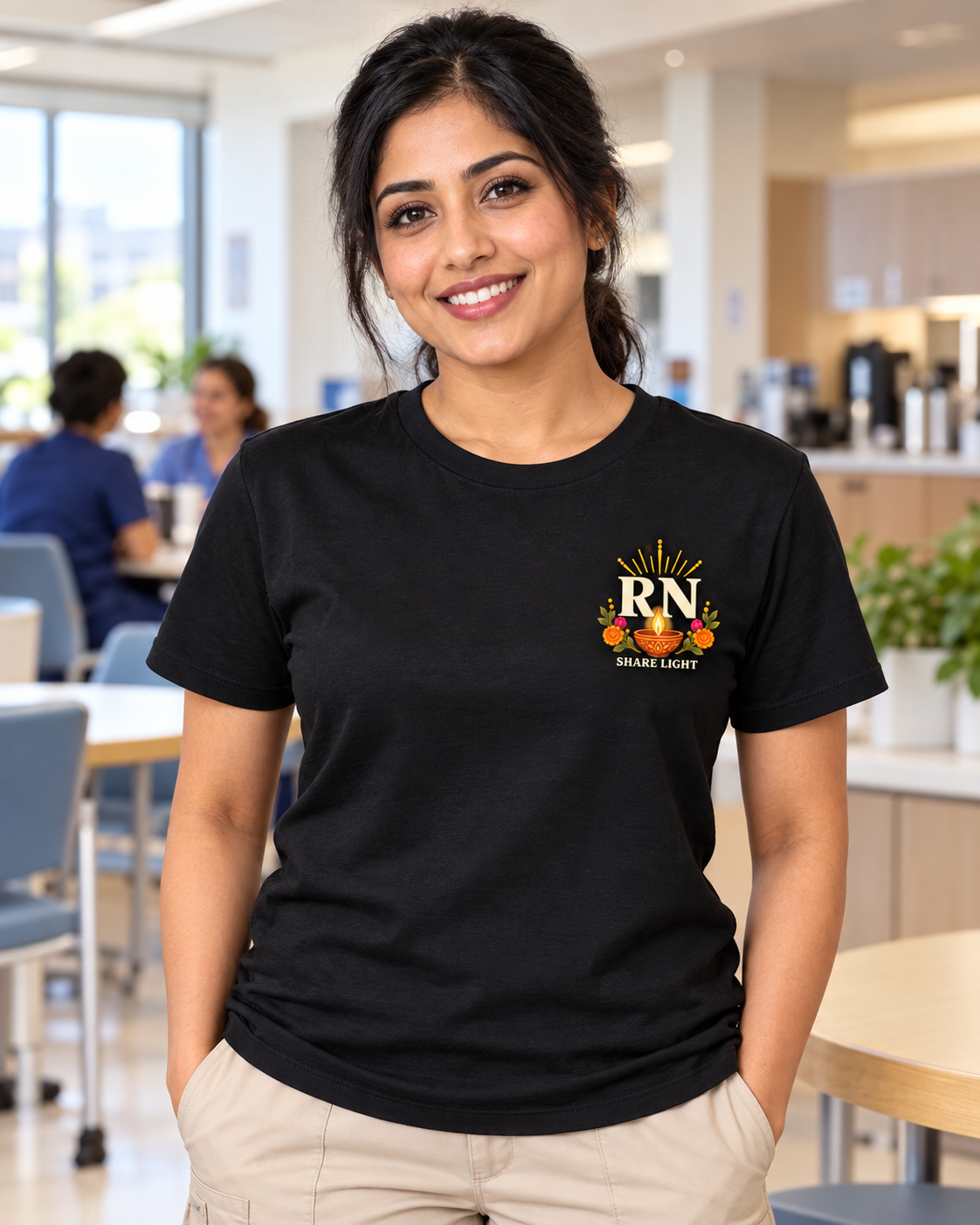Female nurse wearing a black Nursify Diwali T shirt with a small ivory RN, diya lamp and floral design on the left chest, with Share Light beneath.