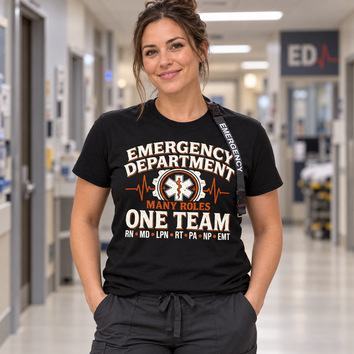 Nurse wearing black Many Roles One Team emergency department shirt with RN MD LPN RT PA NP EMT lettering and Emergency lanyard