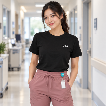 Healthcare worker wearing a black Nursify CCA short sleeve shirt with rose scrub pants and a turquoise CCA badge reel.
