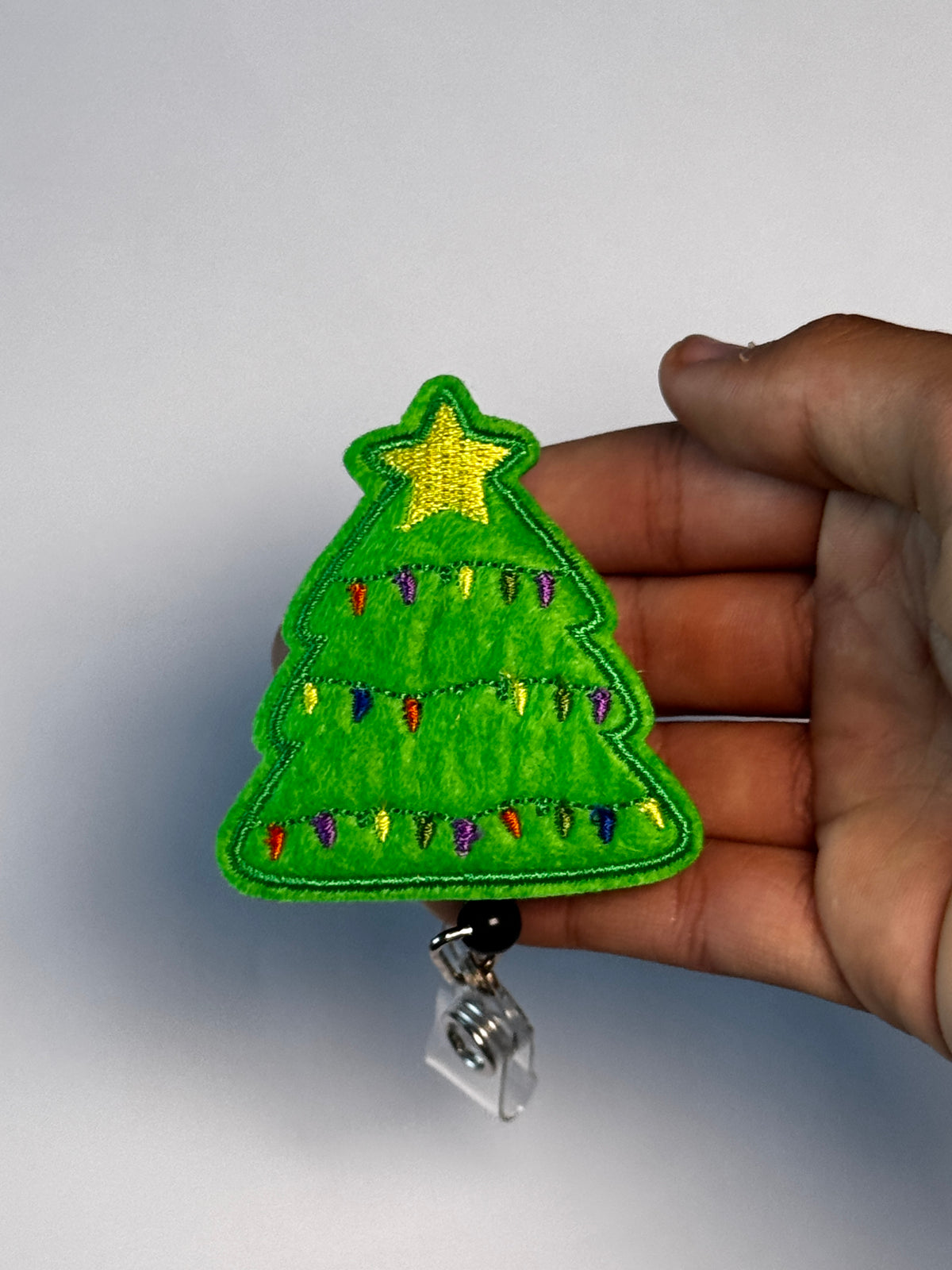 4. Christmas Tree. Actual Christmas Tree Badge Reel held in hand; hand shown for visual reference only