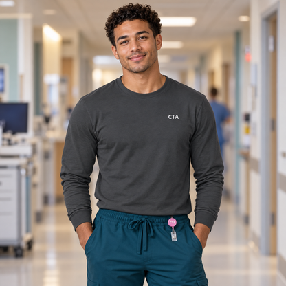 Healthcare worker wearing an asphalt grey Nursify CTA long sleeve shirt with teal scrub pants and a pink CTA badge reel.