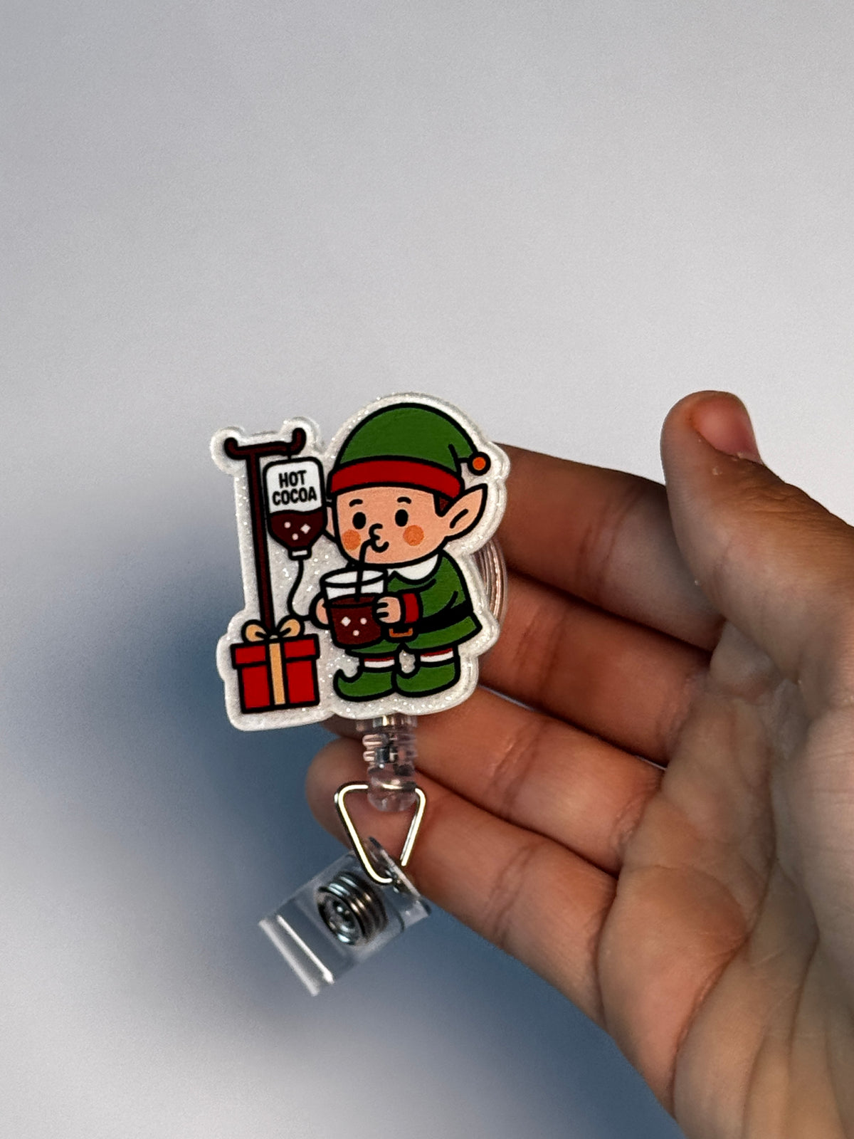 6. Elf with Cocoa IV. Actual Elf with IV Pole Christmas Badge Reel held in hand; hand shown for visual reference only