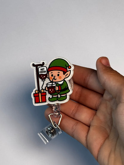6. Elf with Cocoa IV. Actual Elf with IV Pole Christmas Badge Reel held in hand; hand shown for visual reference only