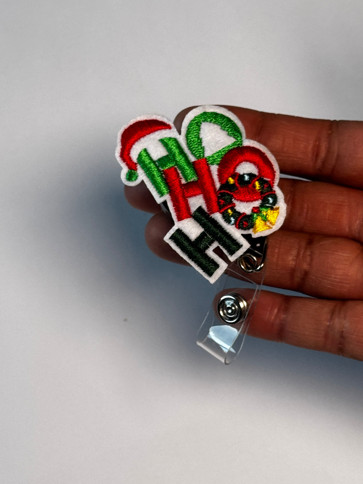 1. Ho Ho Ho. Actual Ho Ho Ho Christmas Badge Reel held in hand; hand shown for visual reference only