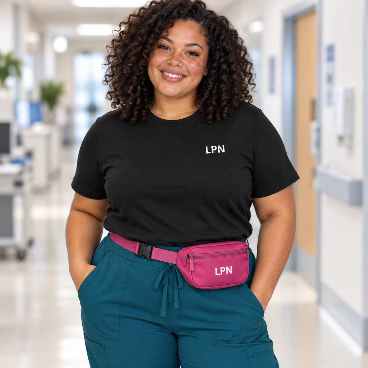 Woman with freckles and curly hair wearing a black Nursify LPN short sleeve shirt, teal scrub pants and a pink LPN waist pack.