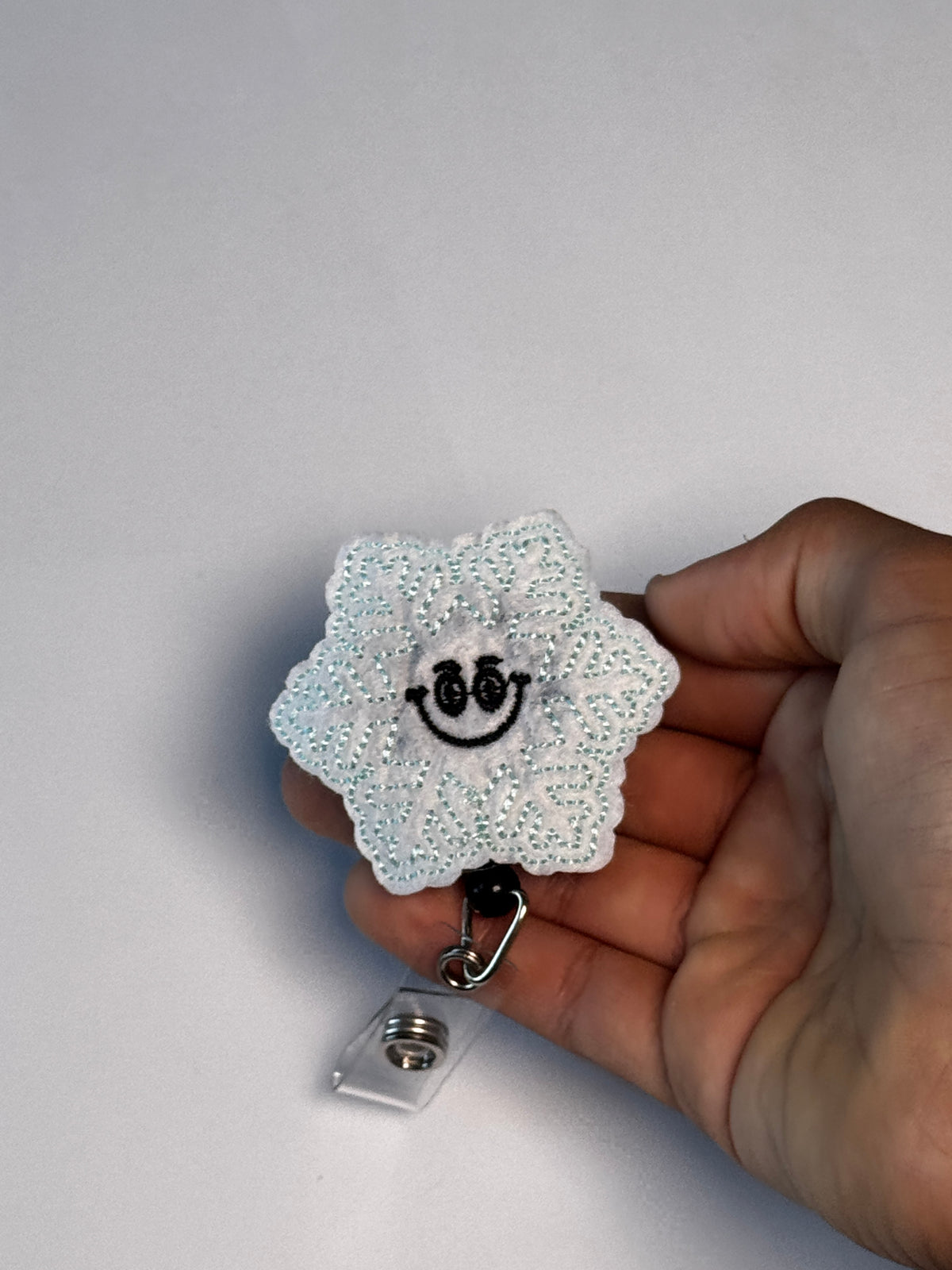 9. Smiling Snowflake. Actual Smiling Snowflake Badge Reel held in hand; hand shown for visual reference only
