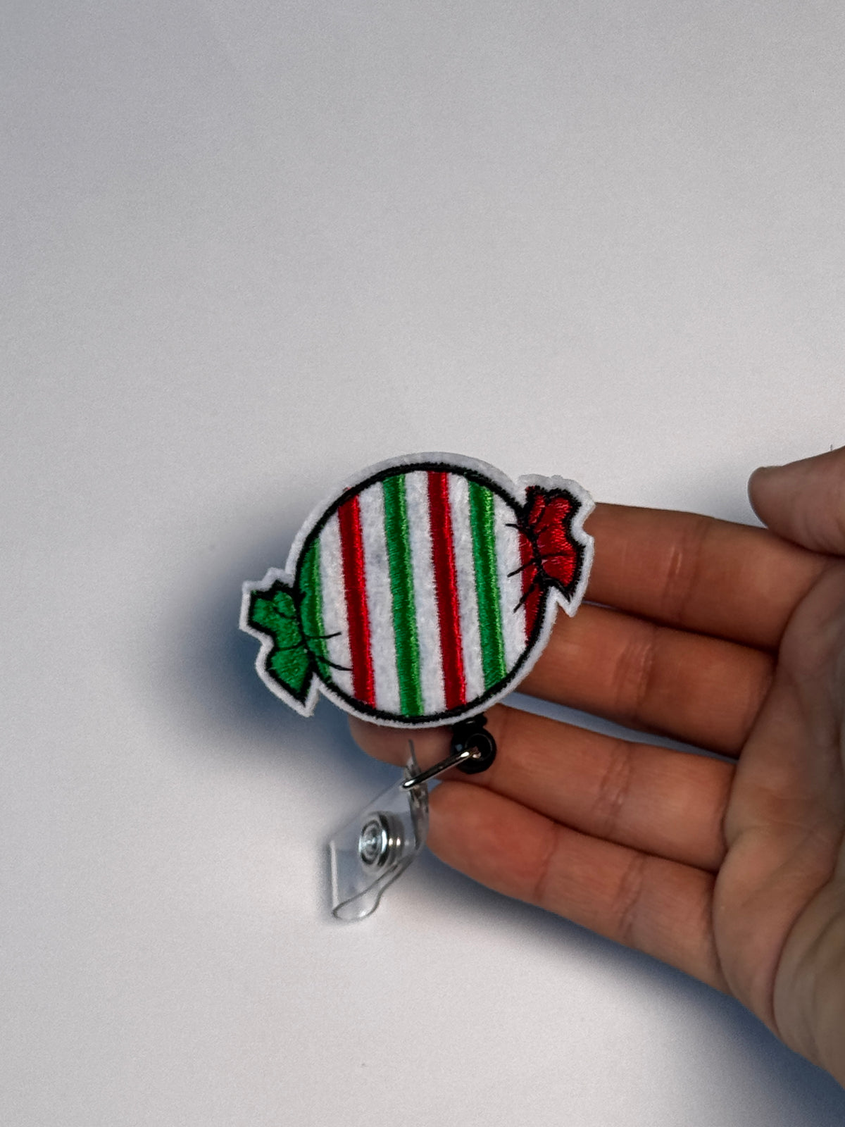 8. Striped Candy. Actual Striped Candy Christmas Badge Reel held in hand; hand shown for visual reference only